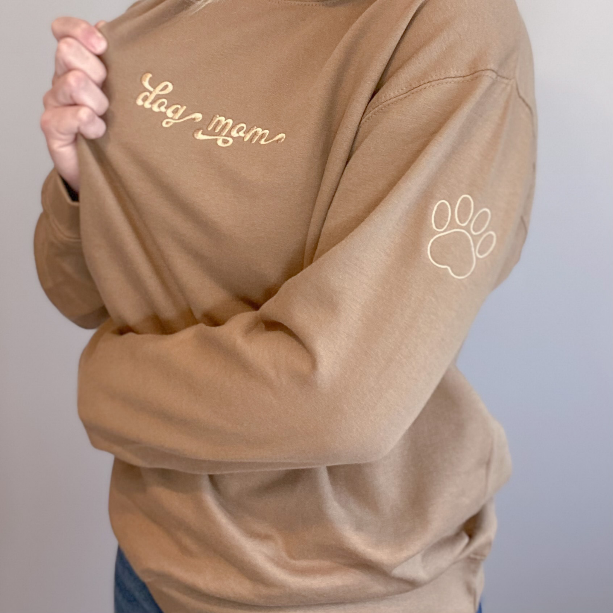 Tan crewneck with dog mom embroidered on the chest and a small paw print embroidered on the sleeve