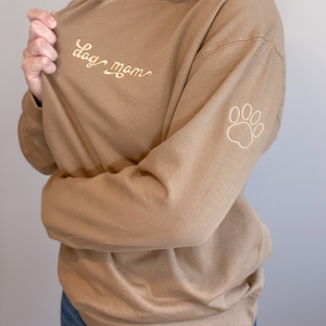 Tan crewneck with dog mom embroidered on the chest and a small paw print embroidered on the sleeve